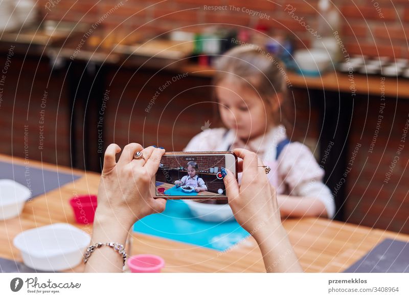 Mutter nimmt ihre kleine Tochter während der Teilnahme am Backworkshop auf. Backkurse für Kinder, aufstrebende kleine Köche. Kochen lernen. Kombinieren und Rühren von zubereiteten Zutaten. Echte Menschen, authentische Situationen