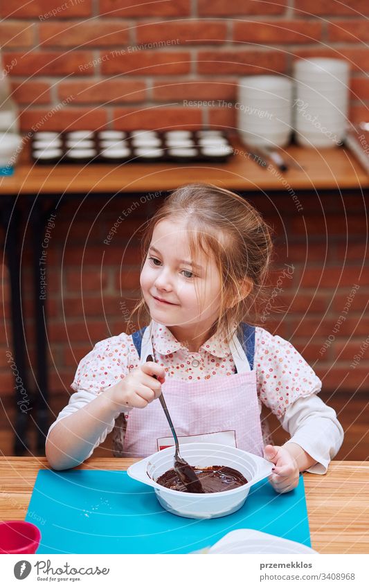 Kleiner Koch, der geschmolzene Schokolade mit Kakao verrührt. Kind, das am Backworkshop teilnimmt. Backkurse für Kinder, aufstrebende kleine Köche. Kochen lernen. Kombinieren und Rühren von zubereiteten Zutaten. Echte Menschen, authentische Situationen