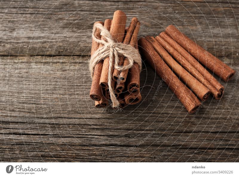 braune Zimtstangen in einem Brötchen gebunden auf grauem Holzgrund, schmackhaftes und duftendes Gewürz Lebensmittel Hintergrund kleben süß hölzern Bestandteil