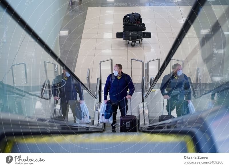 Europäischer Mann mit rotem Bart in blauer Jacke, steigt auf eine Rolltreppe, hat eine medizinische Einweg-Schutzmaske am Flughafen. 2019-ncov ängstlich