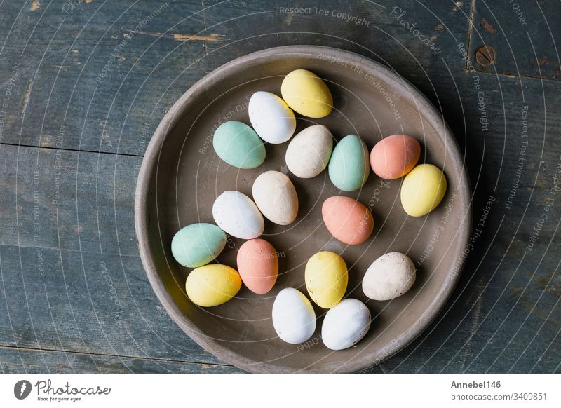 Grauer Keramikteller mit bemalten Ostereiern in Pastellfarben auf altem Holzgrund. Fröhliches Osterkartenkonzept, minimalistisches Design, Ansicht von oben