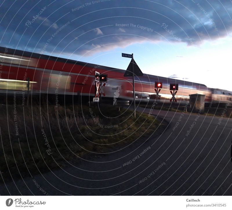 Fahrender Zug am unbeschränkten Bahnübergang Zug, Andreaskreuz, Signal, Bewegung, stopp,frühe Dämmerung Eisenbahn Verkehr Gleise Bahnfahren Außenaufnahme