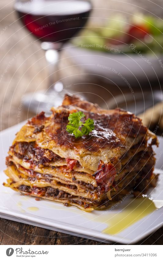 Lasagne auf einem Teller Rotwein Salat grissini Sommer Wein weiß Holz rustikal Hackfleisch Kraut bolognese bolognaise Geschirr gemischt geschmackvoll Mozzarella