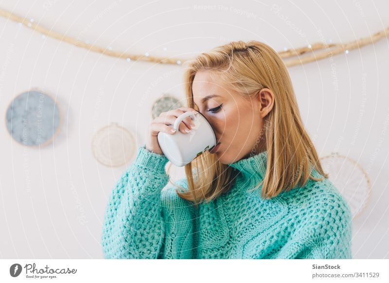 Junges hübsches Mädchen beim Kaffeetrinken Frau Tee jung Tasse Pullover blond Morgen Porträt Glück schön Wand Traumfänger Sonntag Frauen heimwärts Lifestyle