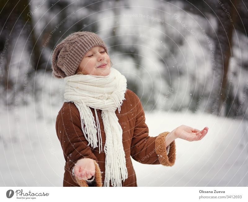 Ein 7-jähriges Mädchen in einem braunen Schafsfellmantel geht im Wald spazieren. Konzept der Jahreszeiten, ein Wintermärchen. Schnee, Bäume. Baby Hintergrund