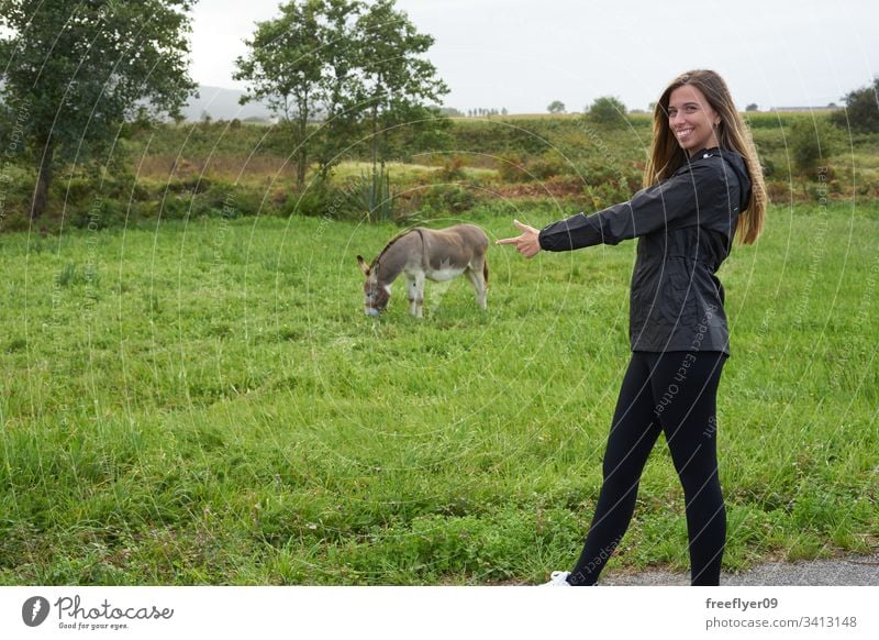 Junge Frau mit einem Esel auf einer Wiese Bauernhof im Freien Lebensmittel Nachkommen Säugetier füttern Aussehen Nutztier niedlich Natur ruhen grün Essen Kopf