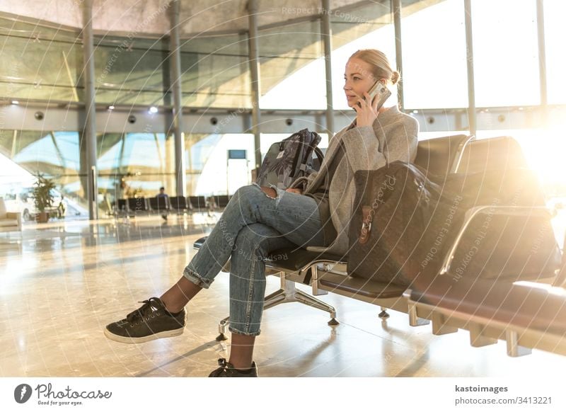 Eine weibliche Reisende, die mit ihrem Handy telefoniert, während sie an den Abfluggates im Flughafen-Terminal auf das Einsteigen in ein Flugzeug wartet. reisen