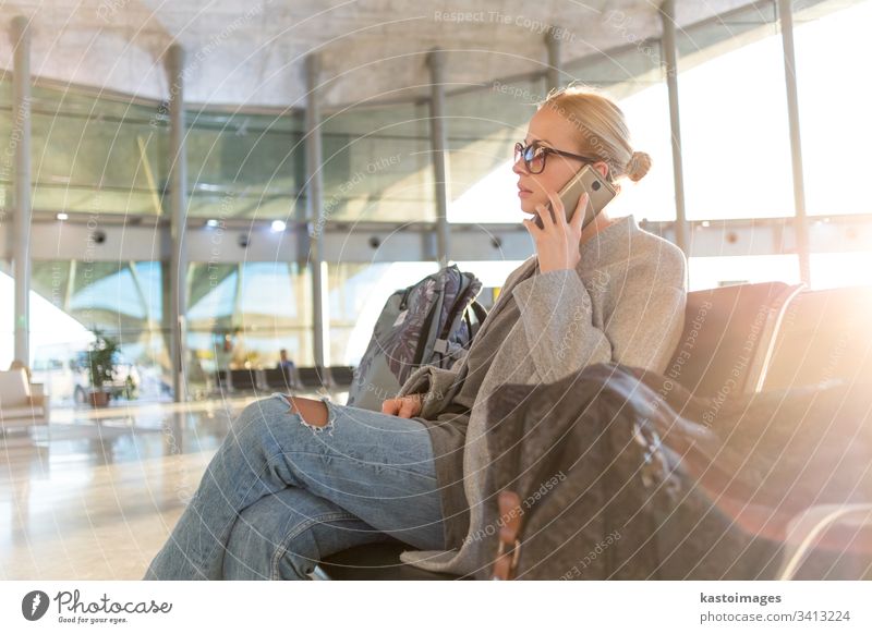 Eine weibliche Reisende, die mit ihrem Handy telefoniert, während sie an den Abfluggates im Flughafen-Terminal auf das Einsteigen in ein Flugzeug wartet. reisen