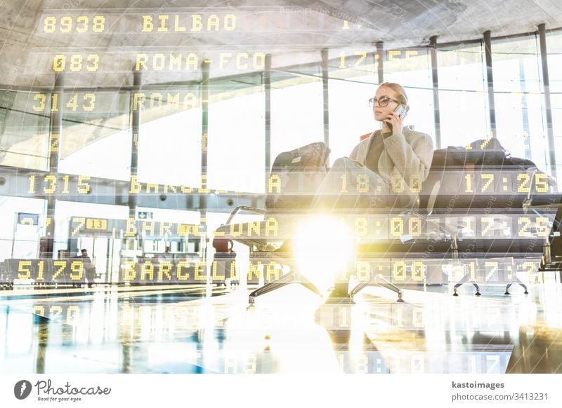 Eine weibliche Reisende, die mit ihrem Handy telefoniert, während sie an den Abfluggates im Flughafen-Terminal auf das Einsteigen in ein Flugzeug wartet. reisen