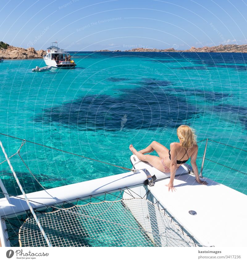 Frau entspannt sich auf einem Sommer-Segeltörn auf einem Luxus-Katamaran in der Nähe des bildschönen weißen Sandstrandes auf der Insel Spargi im Maddalena-Archipel, Sardinien, Italien.