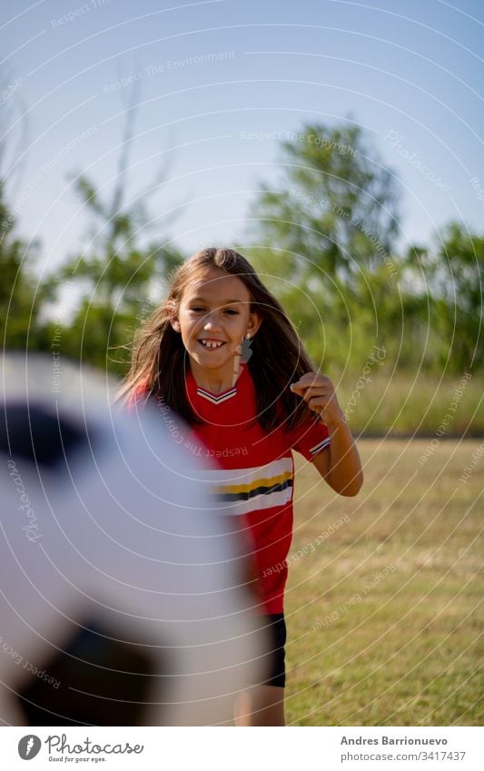 Kleines Mädchen spielt Kind wenig Fußball Jugend Lächeln außerhalb Ball jung Gras Kinder Hände auf den Hüften vertikal im Freien Selektiver Fokus Uniform grün