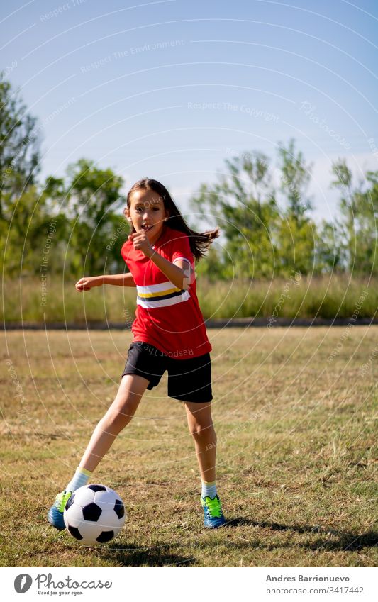 Kleines Mädchen spielt Kind wenig Fußball Jugend Lächeln außerhalb Ball jung Gras Kinder Hände auf den Hüften vertikal im Freien Selektiver Fokus Uniform grün