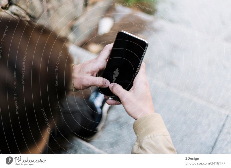 Rückansicht eines jungen Mannes, der im Freien sitzend ein Mobiltelefon benutzt männlich Sitzen 1 Telefon Mobile Beteiligung Menschen photogen modern Typ Person