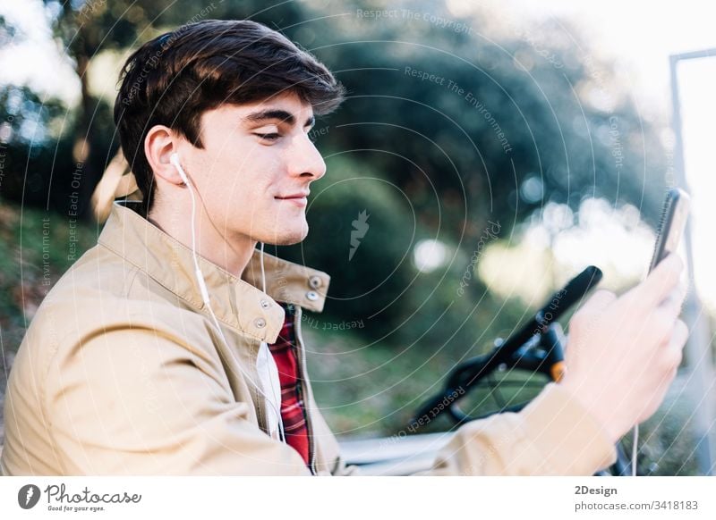 Junger hispanischer Mann, der im Freien sitzend ein Mobiltelefon benutzt männlich Sitzen jung 1 Telefon Mobile Beteiligung Menschen photogen modern Typ Person