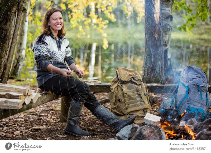 Mann und Frau rösten am Lagerfeuer im Wald am Ufer des Sees, machen ein Feuer, grillen. Ein glückliches Paar erkundet Finnland. Skandinavische Landschaft. aktiv