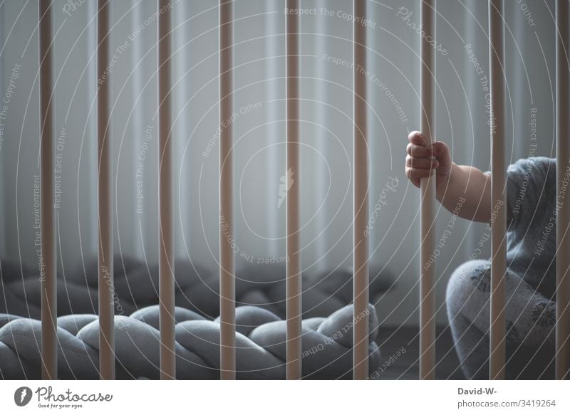 Baby hinter Gittern im Kinderbett Hand klein Junge Kleinkind schlafen wach eingesperrt niedlich festhalten süß alleine Einsam anonym greifen Erziehung