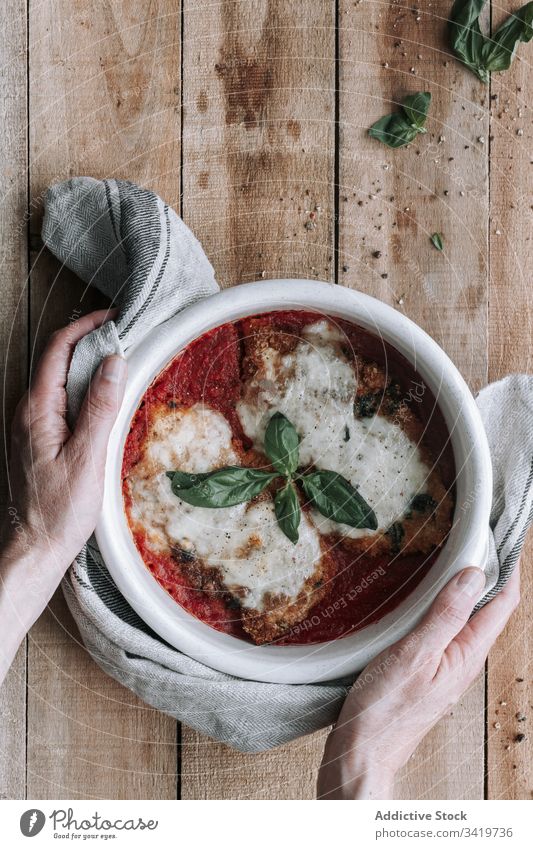 Nicht erkennbare Person, die eine Schüssel voll Huhn mit Käse und Basilikum in Tomatensauce auf den Tisch stellt Speise Utensil Braten Hähnchen Saucen