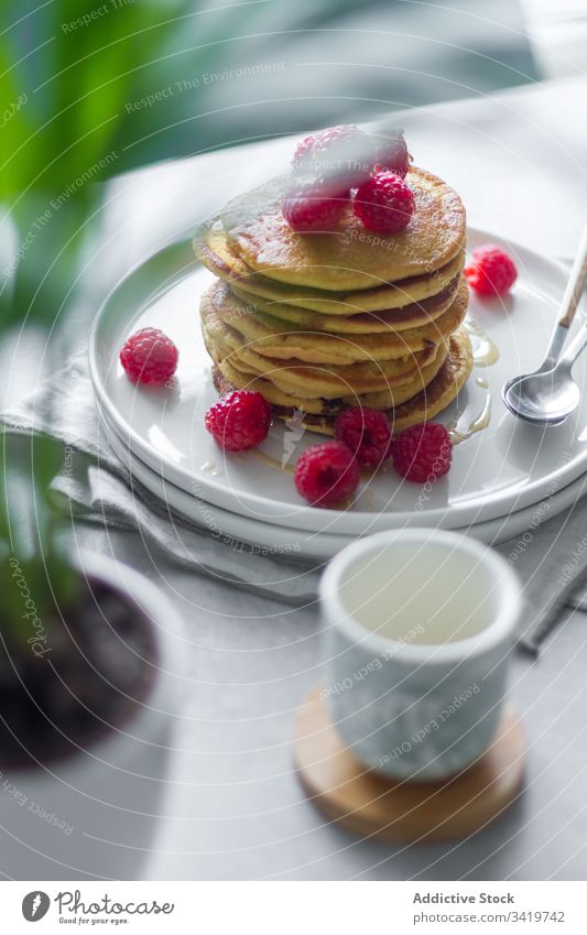 Teller mit Pfannkuchen auf dem Tisch während des Frühstücks Himbeeren Morgen Serviette Tasse Pflanze Topf heimwärts süß Lebensmittel Dessert lecker