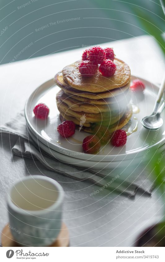 Teller mit Pfannkuchen auf dem Tisch während des Frühstücks Himbeeren Morgen Serviette Tasse Pflanze Topf heimwärts süß Lebensmittel Dessert lecker