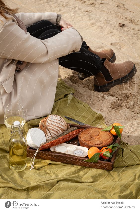 Erntehelferin sitzt neben Wein und Tablett mit Gebäck und Mandarinen mit Würstchen und Käse Frau Picknick Strand Lebensmittel Decke ruhen Sand sitzen Brot