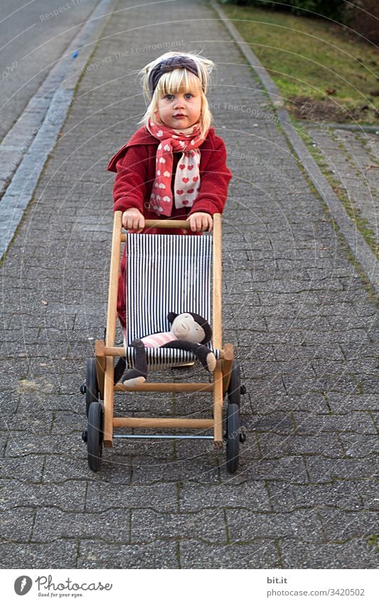 Der Affe liegt bequem, freut sich das Mädchen und schiebt den Puppenwagen über den Gehweg. Kindheit puppenwagen Spaziergang gehweg schieben Spielen Glück