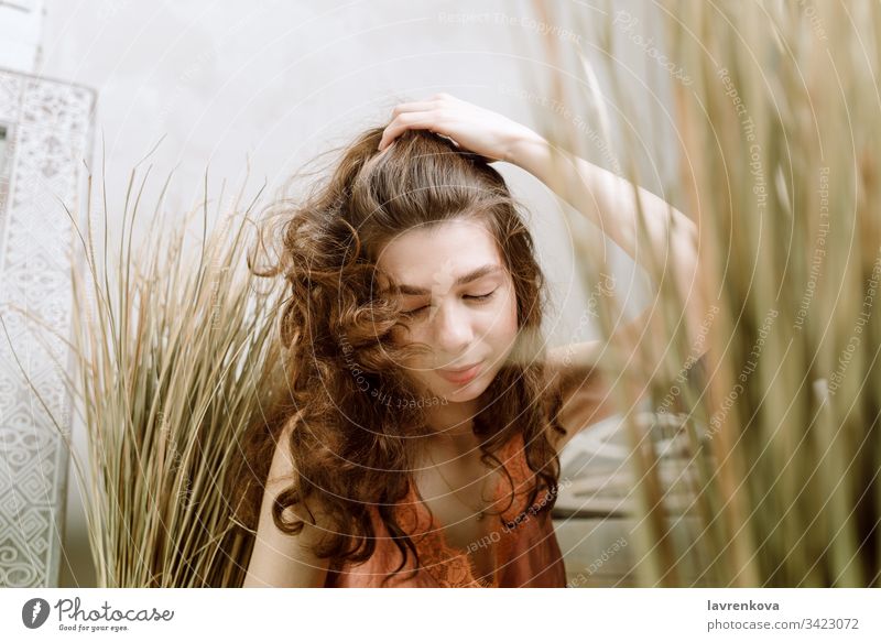 Junge brünette Frau, die den Kopf schüttelt und sich die Haare leckt, selektiver Fokus lockig lässig Kopfschütteln Gras Licht heiter Kaukasier Lifestyle