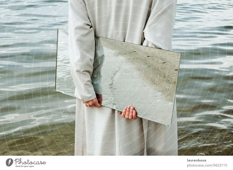 Nahaufnahme einer Frau in blauem Kleid, die am Ufer steht und einen Spiegel hält, in dem sich der Strand spiegelt, selektiv Erwachsener Kaukasier Sauberkeit