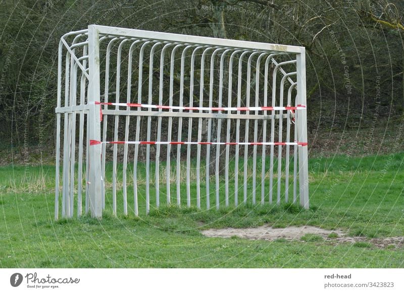 Metallfussballtor auf dem Fussballfeld, das wegen Corona mit einem Flatterband geschlossen wurde Fußballtor gesperrt grün Spielplatz Fußballfeld Tor im Freien