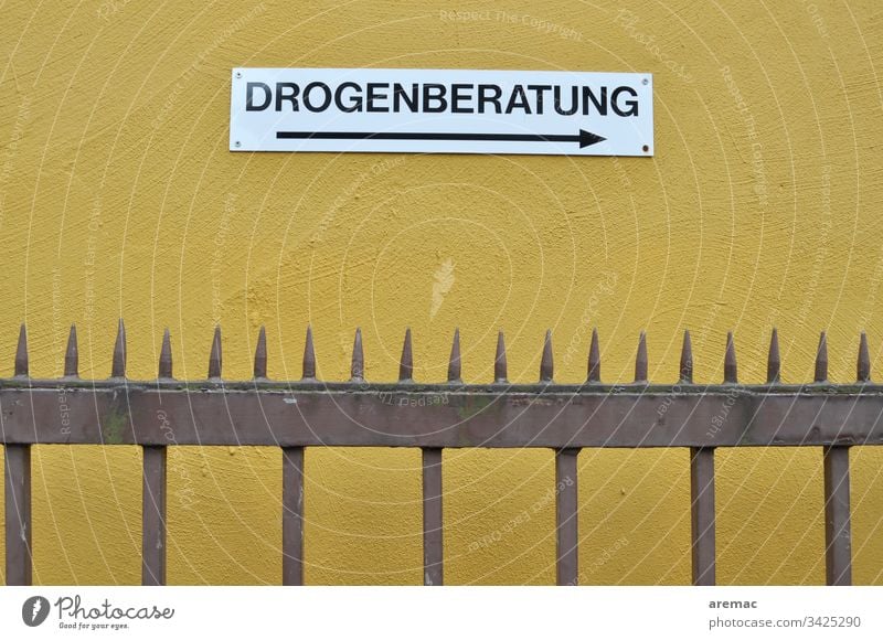 Schild Drogenberatung an einer gelben Wand Beratung Zaun Metall Spitzen Außenaufnahme Hinweisschild Schilder & Markierungen Mauer Buchstaben weiß