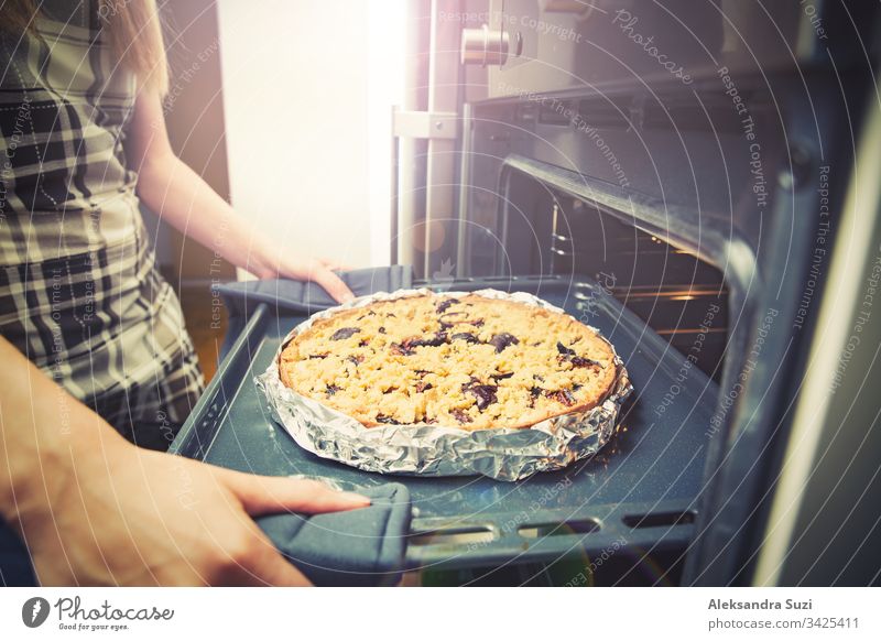 Frauenhände beim Herausnehmen des Tabletts mit Gebäck aus dem Ofen, Nahaufnahme. Frischer hausgemachter köstlicher Pflaumenkuchen. backen Kuchen Koch