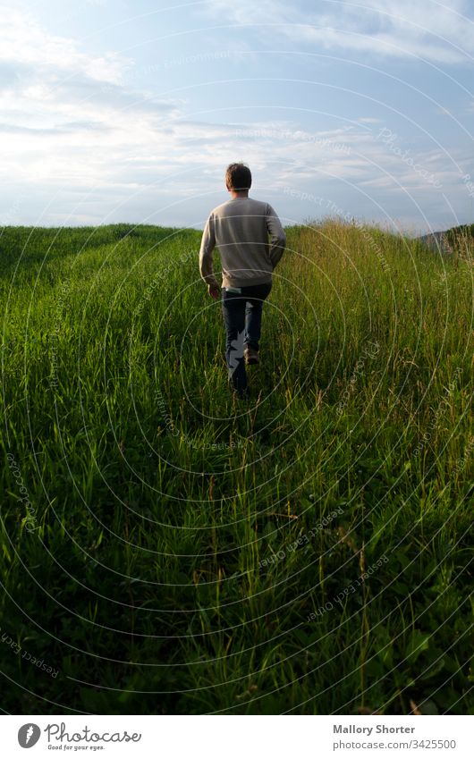 Mann geht bei Sonnenuntergang durch grasbewachsene Hügel laufen weggehend Feld Rasenfläche reisen erkunden Wiese Junge männlich Sonnenaufgang Natur