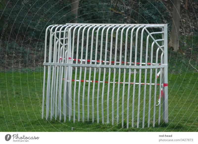 Metallfussballtor von hinten auf dem Fussballfeld, das wegen Corona mit einem Flatterband geschlossen wurde Fußballtor gesperrt grün Spielplatz Fußballfeld Tor