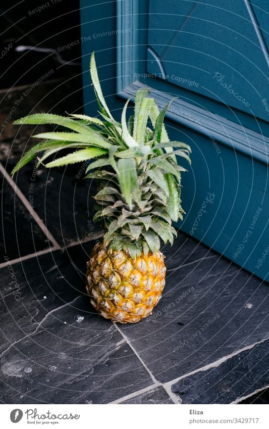 Eine ganze Ananas die auf dem Boden vor einer Tür steht Frucht gesund lecker exotisch blau Geschenk mitbringen grün gelb Ananasblätter Obst frisch Farbfoto süß