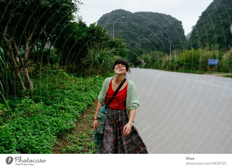 Eine junge Frau in bunter Kleidung, die eine leere Straße in Asien entlangläuft und lächelt Touristin Tourismus Südostasien Lebensfreude Reisen Urlaub