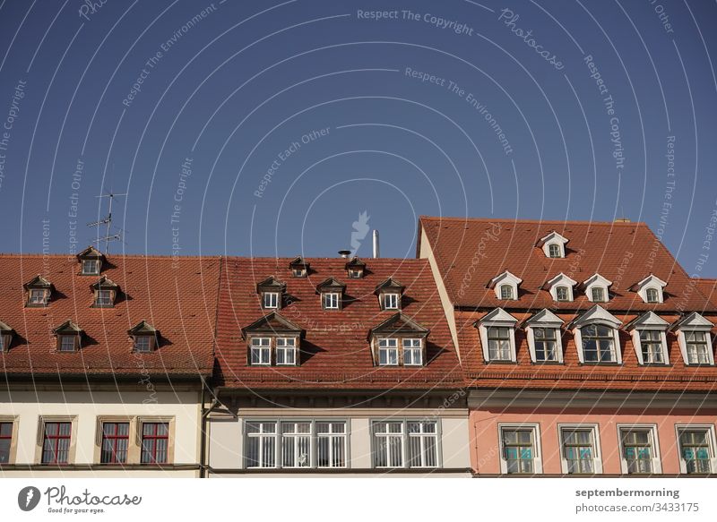 drei Häuserdächer mit verschieden großen Fenstern darin eine Fensterzeile kleine Fenster im Dach blauer Himmel 3 Schindeldächer rot Fenster mit Streben