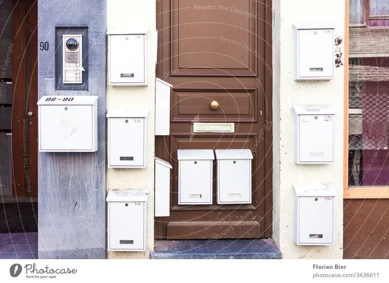 Aussen angebrachte Briefkästen an einem Wohnhaus mit Eingangstüre Briefkasten Briefkastenschlitz Post Tür Haus schreiben Stadt Metall Wand Fassade Gebäude