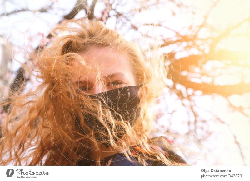 Mädchen mit medizinischer Maske auf einem Hintergrund mit blühenden Bäumen. Die Maske ist schwarz. Schutz gegen Virus, Grippe. Frühlingsallergie Mundschutz