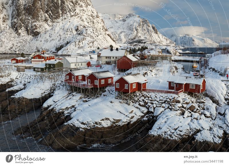 Hamnoy auf den Lofoten mit Aussicht auf die kleinen roten Häuschen die auf verschneiten Felsen stehen Panorama (Aussicht) Reinefjorden Fjord Küste bewölkt