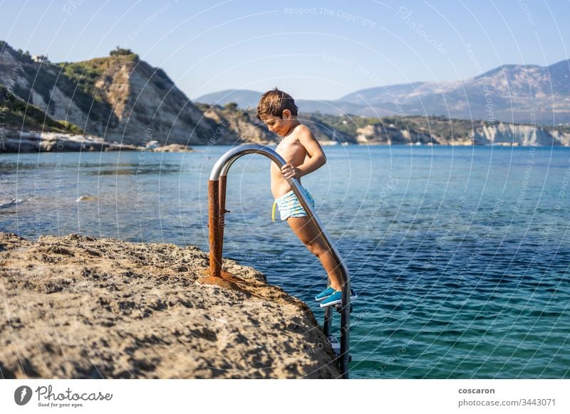 Kleiner Junge auf einer Badeleiter, der zum Baden ins Meer hinuntergeht amandakis schön blau Kind Kindheit übersichtlich Klettern Küste Kristalle niedlich