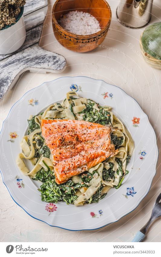 Teller mit Nudeln, Lachs und Spinat auf weißem rustikalem Tischfond. Gesunde Mahlzeit. Diät. Mittagessen. Ansicht von oben Hintergrund Gesundheit Lebensmittel