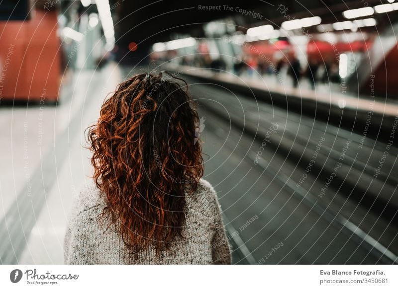 junge, schöne Frau am Bahnhof mit dem Handy, bevor sie den Zug erreicht. Ansicht von hinten. Reise-, Technologie- und Lifestyle-Konzept reisen Station bewegend