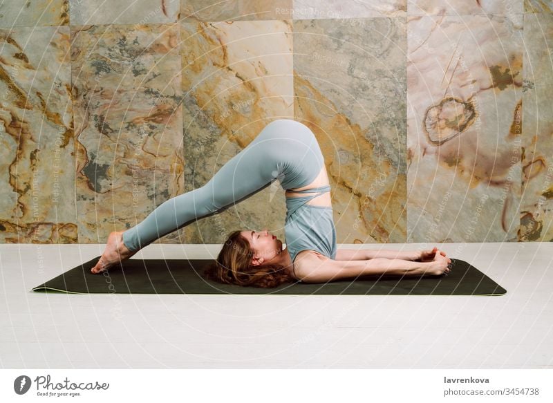 Junge Yogini übt Halasana (Pflug-Pose) in pastellblauen Leggins und oben, selektiver Fokus Pflug-Position aktiv Asana Athlet sportlich attraktiv Körper brünett