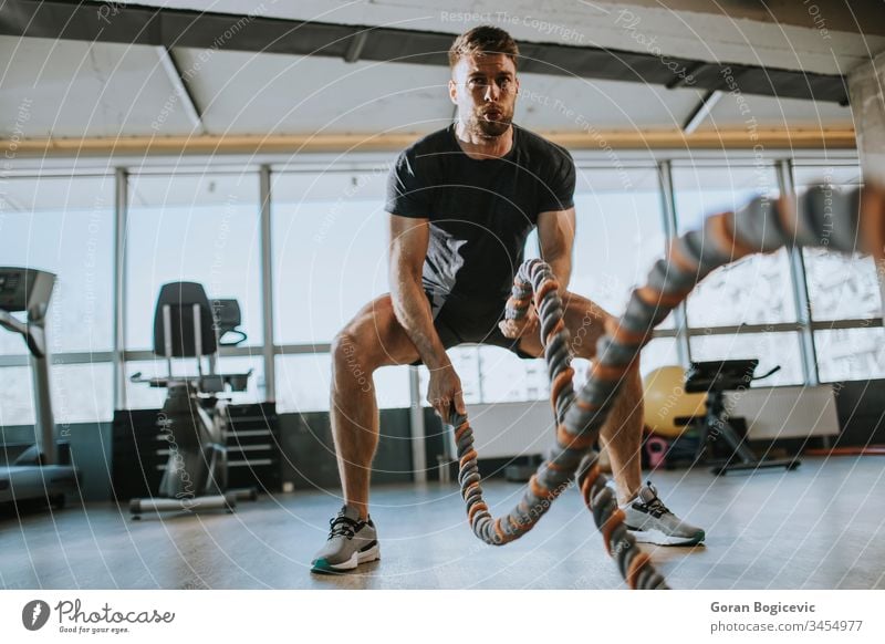 Junger Mann übt mit Kampfseilen in der Turnhalle muskulös Stärke Fitness Schlacht Training Gesundheit Fitnessstudio Sport männlich stark jung Übung Körper