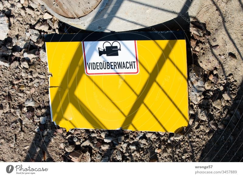 Gelbes Hinweisschild Videoüberwacht liegt auf dem Boden einer Baustelle Schotter Außenaufnahme Menschenleer Tag Farbfoto Arbeit & Erwerbstätigkeit Arbeitsplatz