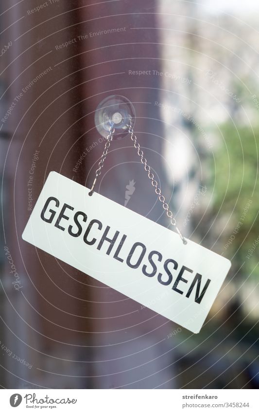 Schild „Geschlossen“ hängt an einer Glasscheibe, in der sich die Umgebung spiegelt Laden Geschäft geschlossen Gebäude Corona Corona-Virus Krise Coronakrise