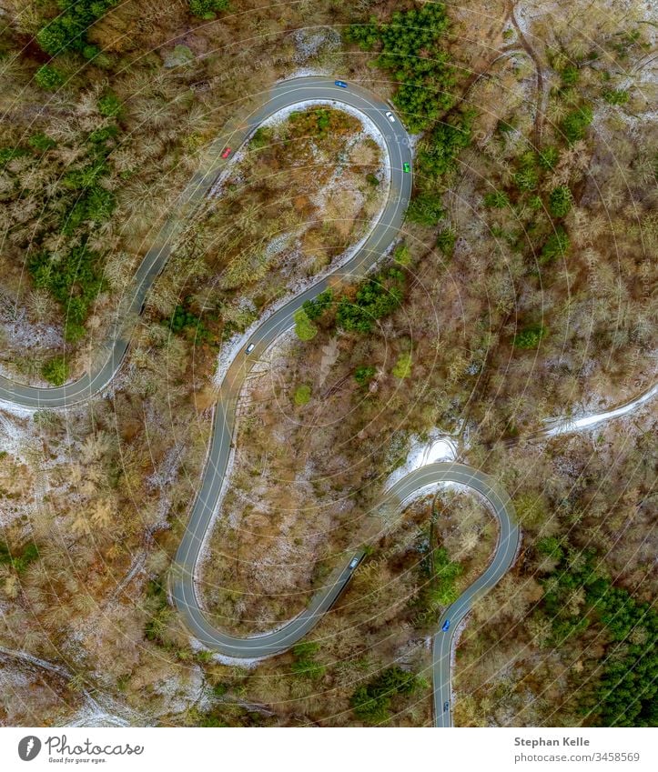 Eine kurvige Straße aufgenommen mit einer Drohne von oben mit fahrenden Autos im Winter mit teilweise liegendem Schnee. Luftaufnahme Außenaufnahme Tag