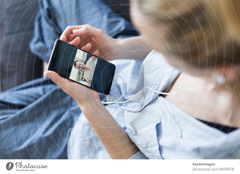 Frau zu Hause, die sich auf der Couch entspannt und während der Coronavirus-Pandemie soziale Medien am Telefon für Video-Chats mit ihren Lieben nutzt. Zu Hause bleiben, sozial distanzierender Lebensstil.