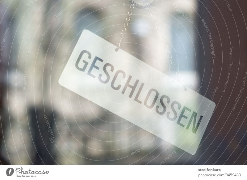 „Geschlossen“ steht auf dem Schild, das innen an der Glastür hängt, während sich die Umgebung im Glas spiegelt Laden Geschäft geschlossen Gebäude Corona