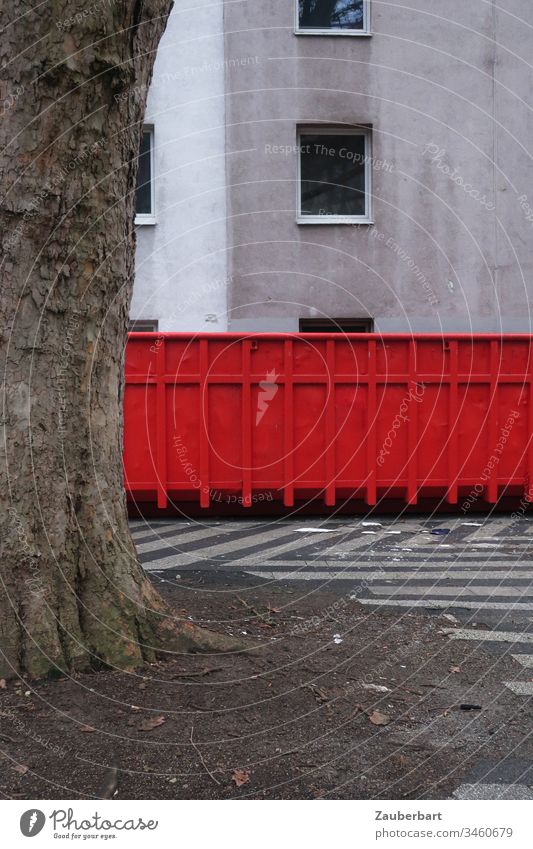 Roter Container steht vor trister Hausfassade mit leerem Fenster, davor ein Baum rot Baumstamm Ausgangssperre Fassade grau Menschenleer Tag Gebäude Bauwerk