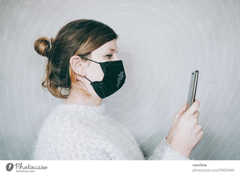 Junge Frau, die eine Maske trägt, während sie ihr Smartphone benutzt Bund 19 COVID Coronavirus Virus Atem Pandemie Mundschutz Krankheit infiziert Mobile Telefon